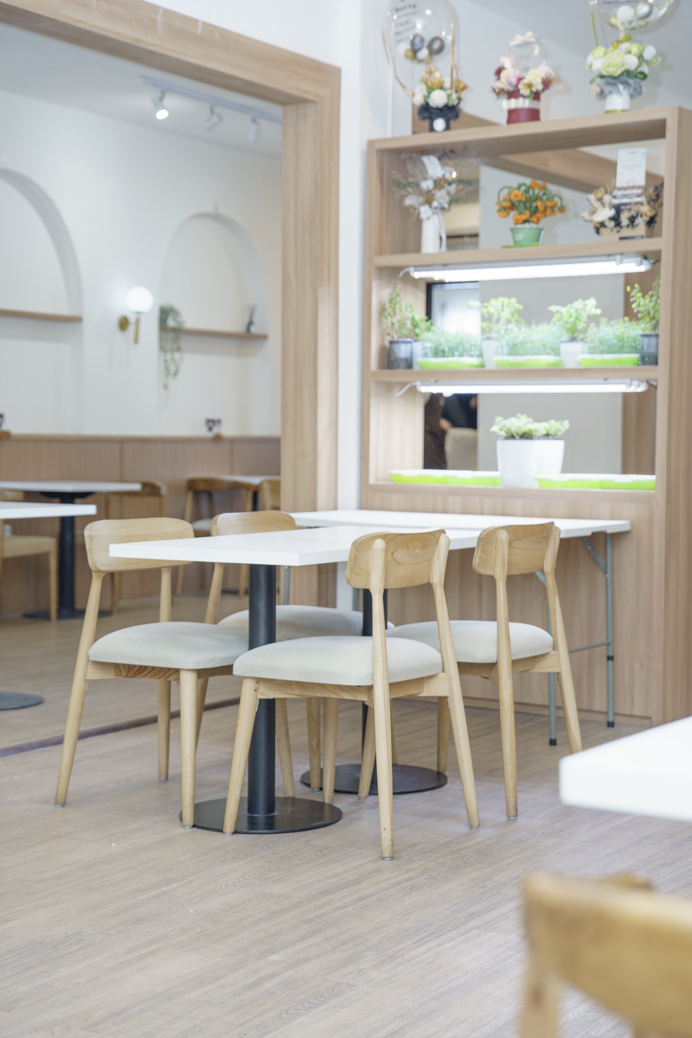 Light-wood tables and chairs beside the planted shelving